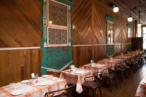 Interior of a cozy restaurant with wooden walls, checkered tablecloths, and decorative windows.