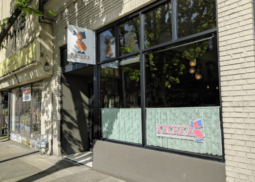 Exterior of Rachka restaurant with large windows, a sign featuring a cartoon fox, and green curtains.