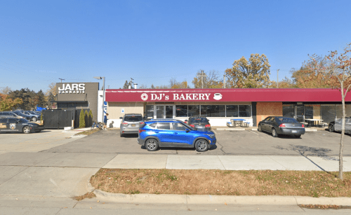 A blue SUV parked in front of DJ's Bakery, with Jars Cannabis visible on the left and clear blue skies above.