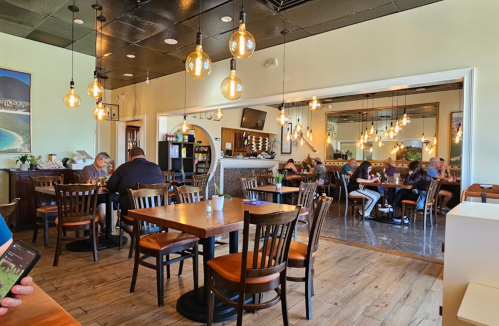A cozy restaurant interior with wooden tables, pendant lights, and diners enjoying their meals in a warm atmosphere.