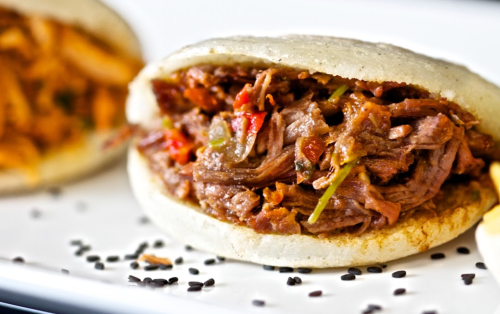 Close-up of a savory arepa filled with shredded beef and colorful vegetables, served on a white plate.