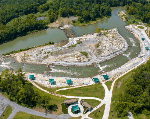 Aerial view of a river landscape with rocky banks, green trees, and picnic areas along the water's edge.