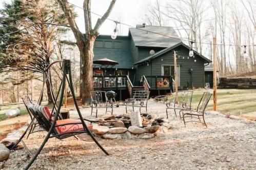 A cozy outdoor seating area with a fire pit, surrounded by trees and a dark house in the background.