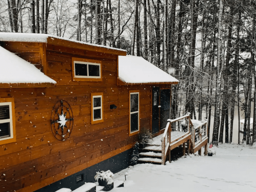 A cozy wooden cabin covered in snow, surrounded by tall trees in a winter landscape.
