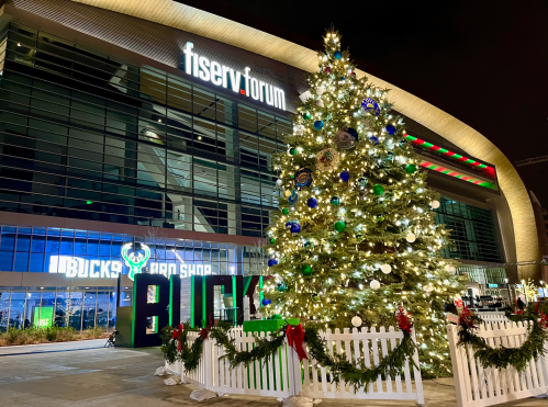 A festive Christmas tree adorned with lights stands outside the Fiserv Forum, decorated for the holiday season.