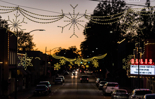 A street decorated with festive lights and snowflake designs, illuminated against a sunset sky.