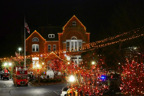 A festive scene of a building adorned with colorful lights, surrounded by trees and decorations, at night.