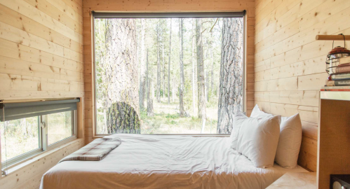 Cozy wooden bedroom with a large window overlooking a forested landscape.