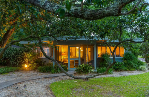 A cozy house surrounded by greenery, illuminated warmly at dusk, with a winding path leading to the entrance.