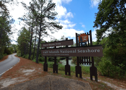 Sign for Davis Bayou Area at Gulf Islands National Seashore, surrounded by trees and a scenic road.