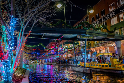 A vibrant canal scene at night, adorned with colorful lights and festive decorations, bustling with people and activity.