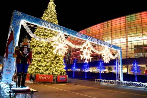 A festive scene featuring a large Christmas tree, snowflake decorations, and a nutcracker statue under bright lights.