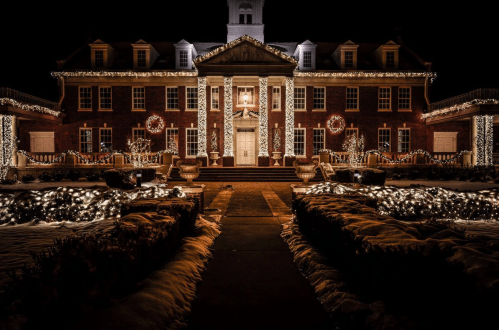 A beautifully lit historic building adorned with holiday lights and decorations, surrounded by snow-covered landscaping.