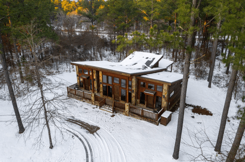 Aerial view of a wooden cabin surrounded by snow-covered trees in a winter landscape.