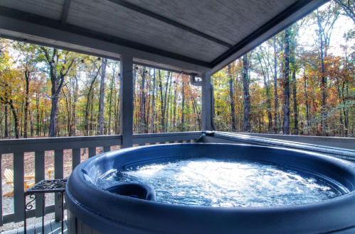 A hot tub on a deck surrounded by trees with autumn foliage, under a covered area.