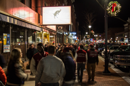 Crowd of people walking past a restaurant at night, with festive decorations and lights along the street.