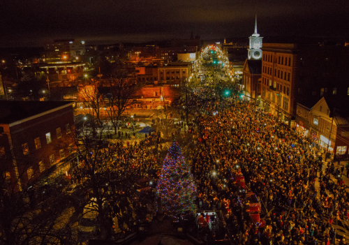 Aerial view of a large crowd gathered for a festive event, with a brightly lit Christmas tree and city lights in the background.