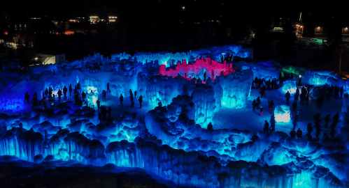 Aerial view of an illuminated ice sculpture park with colorful lights and visitors exploring the icy formations.