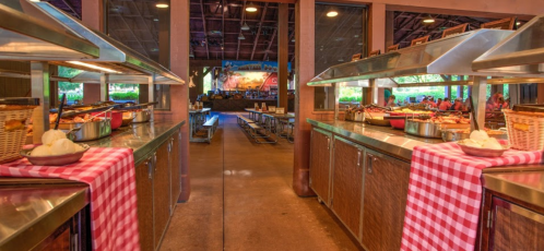 Buffet setup with stainless steel counters, checkered tablecloths, and a spacious dining area in a rustic venue.