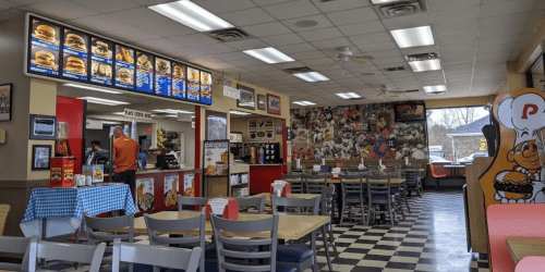 Interior of a fast-food restaurant with a checkered floor, menu boards, and customers ordering at the counter.