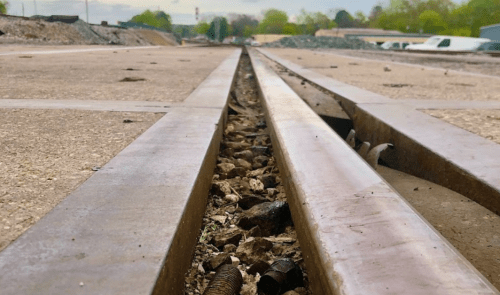 Close-up of railway tracks with gravel and debris between the rails, set against a cloudy sky.