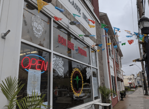 A restaurant exterior with an "OPEN" sign, colorful banners, and decorative window art on a cloudy day.