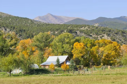 A scenic view of a rustic house surrounded by colorful autumn trees and mountains in the background.