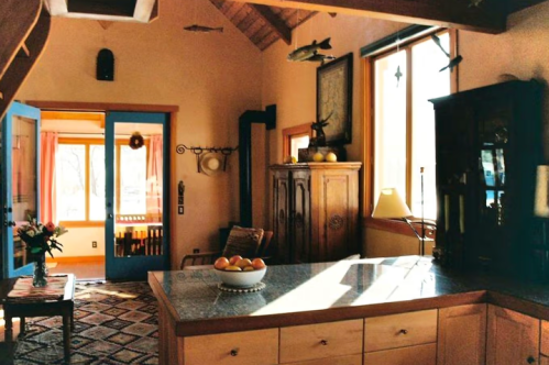 Bright kitchen with wooden cabinets, a marble island, and large windows, featuring a cozy seating area and decorative fish.