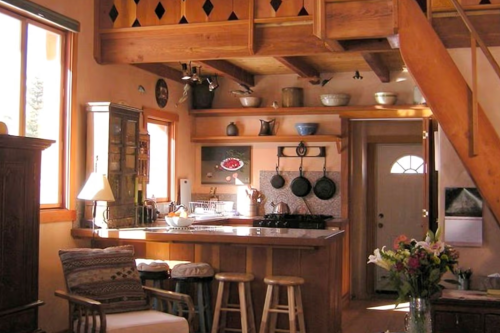 Cozy kitchen with wooden shelves, pots, and a bar area, featuring warm lighting and rustic decor.