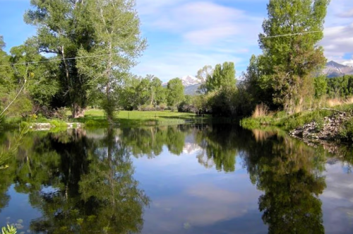 A serene landscape featuring a calm river reflecting trees and mountains under a clear blue sky.