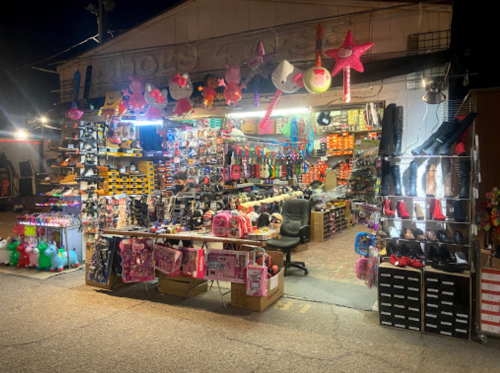 A brightly lit night market stall filled with colorful toys, shoes, and accessories, showcasing a variety of items for sale.