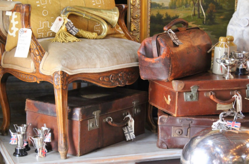 A vintage chair beside stacked leather suitcases and trophies, showcasing a mix of antique items in a cozy setting.