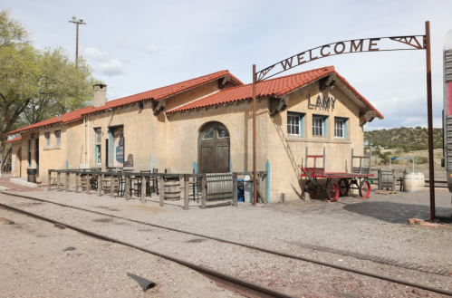 Historic train station with a "Welcome" sign, outdoor seating, and rustic architecture in a desert landscape.