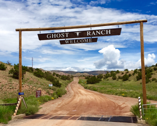 A wooden sign reading "Welcome to Ghost Ranch" over a dirt road surrounded by green hills and blue skies.