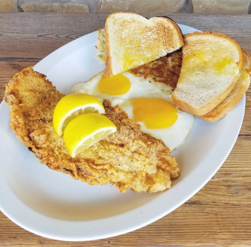 A plate of fried fish with two lemon wedges, sunny-side-up eggs, and toasted bread.