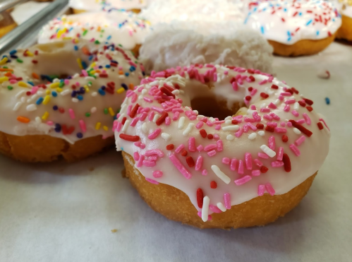 A close-up of two donuts: one with pink icing and sprinkles, and another with white icing and coconut flakes.
