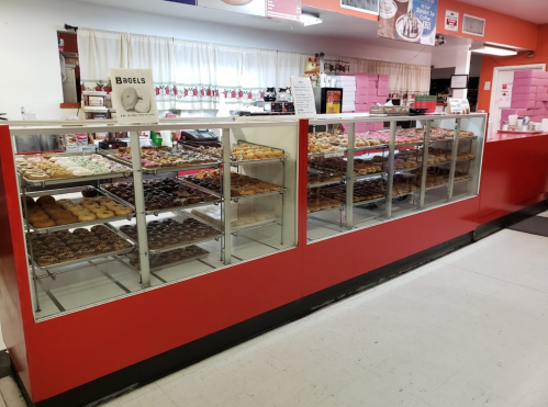 A display case filled with various donuts and pastries in a bakery, with a red counter and a sign for bagels.