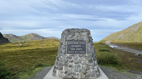Stone monument at Hatcher Pass Summit, 3886 feet above sea level, surrounded by mountains and open landscape.