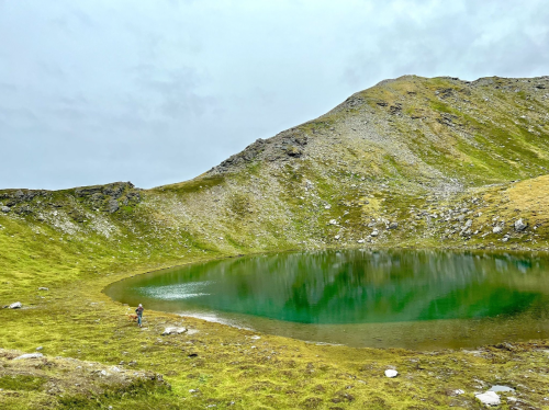 A serene landscape featuring a small green lake surrounded by rocky hills and grassy terrain under a cloudy sky.