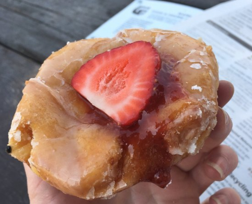 A hand holding a glazed pastry topped with a slice of strawberry and a layer of fruit jam.