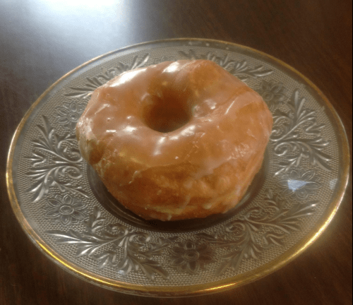 A glazed donut on a decorative glass plate, resting on a wooden table.