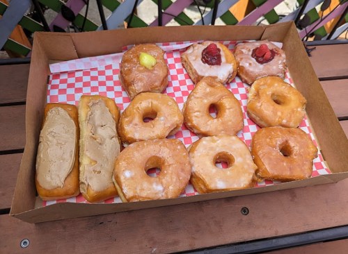 A box of assorted donuts, including glazed, filled, and topped varieties, arranged on a checkered paper.