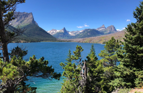 A serene lake surrounded by lush trees and majestic mountains under a clear blue sky.