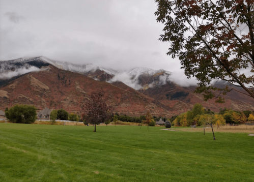 Cloudy mountains with autumn foliage and a grassy field in the foreground, creating a serene landscape.