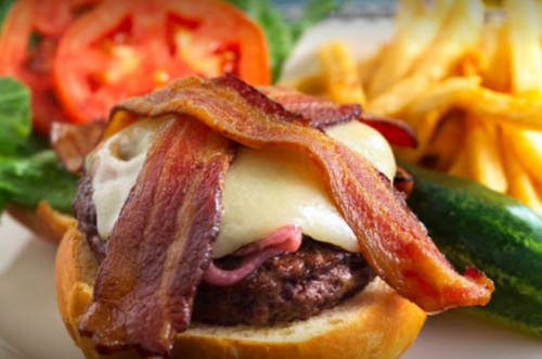 A close-up of a burger topped with bacon and cheese, served with lettuce, tomato, and a side of fries.