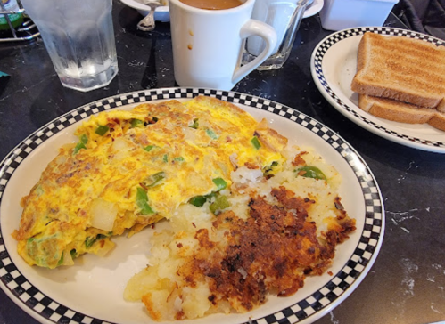 A plate with a vegetable omelette, crispy hash browns, toast, and a cup of coffee in the background.