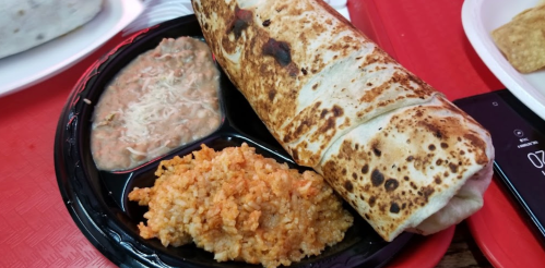 A plate featuring a large burrito, rice, and refried beans, served on a red tray.