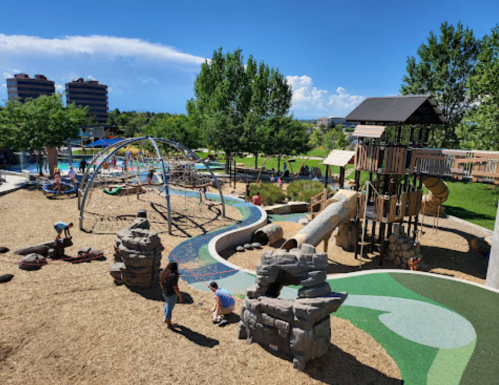 A vibrant playground with climbing structures, slides, and children playing on a sunny day, surrounded by greenery.