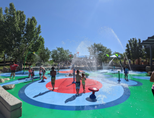 Children playing in a colorful splash pad, enjoying water features under a clear blue sky.