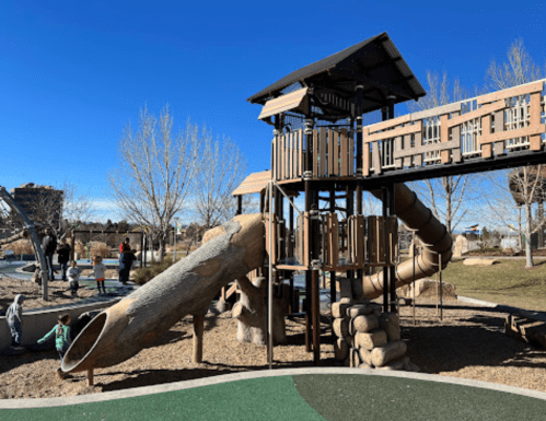 A playground with a wooden structure, slide, and climbing features, set against a clear blue sky.
